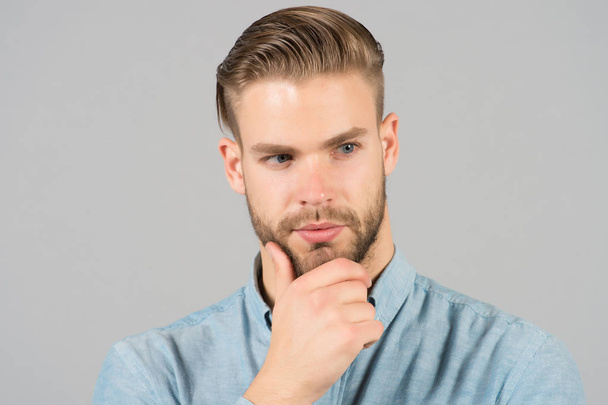 Macho with stylish hair touch beard with hand. Bearded man with healthy young skin. Guy with unshaven face and mustache. Beard grooming and hair care in barbershop. Skincare and mens beauty concept - Foto, Imagen