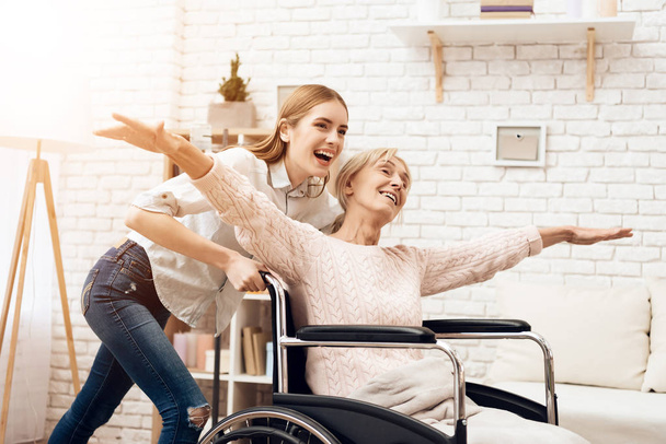 Girl nursing elderly woman and riding her in wheelchair - Photo, image