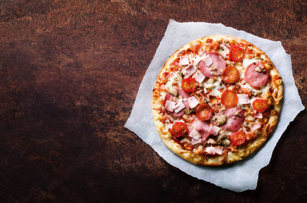Fresh italian pizza with mushrooms, ham, tomatoes, cheese on on backing paper, dark background. Copy space. Homemade with love. Fast delivery. Recipe and menu. Top view. - Fotó, kép