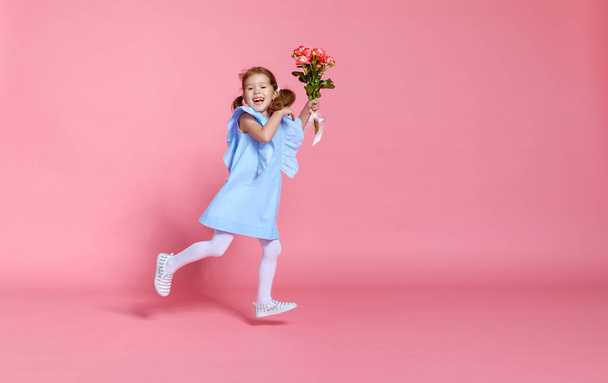grappige kind meisje loopt en springt met boeket bloemen op kleur - Foto, afbeelding