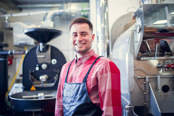 Picture of young man in apron on background of industrial coffee grinder - Zdjęcie, obraz