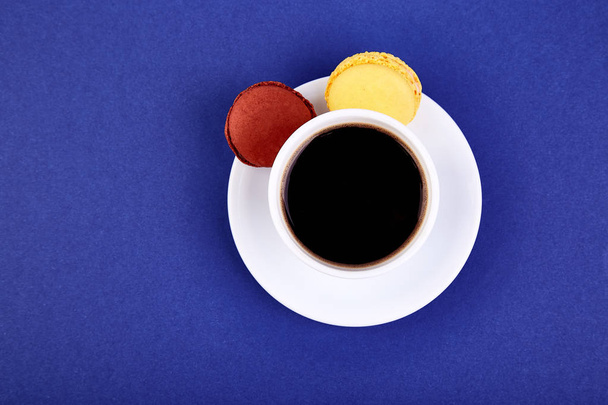 Γλυκό επιδόρπιο Macaron ή αμυγδαλωτό με καφέ σε κίτρινο φόντο, χρωματιστά μπισκότα, κέικ. Καλημέρα, το πρωινό. Την άνοιξη. Επίπεδη θέσει. Αντιγράψτε το χώρο. Μινιμαλισμός - Φωτογραφία, εικόνα