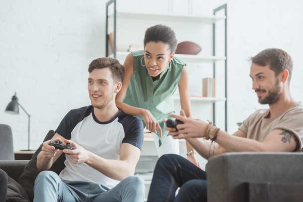 young african american woman watching two men playing video game with joysticks in hands - Фото, зображення