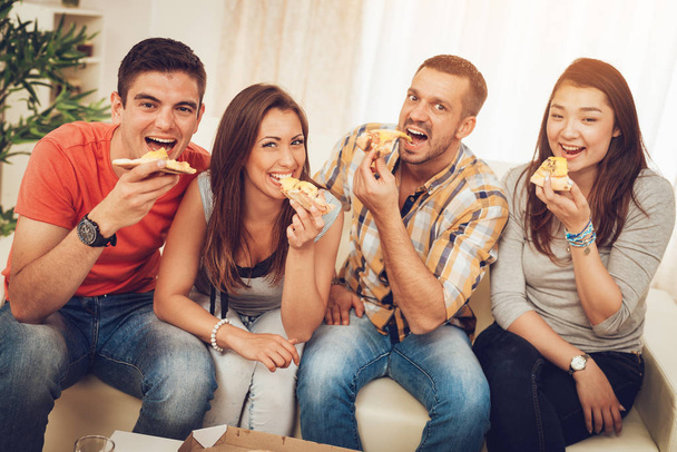 Quatre amis joyeux appréciant la pizza ensemble à la fête à la maison
 - Photo, image