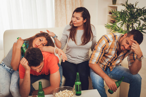 Cuatro jóvenes amigos borrachos sentados en el sofá y resaca después de la fiesta de la casa
 - Foto, imagen