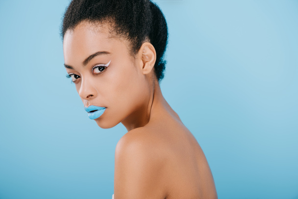 seductive young woman with creative makeup and blue lips looking at camera isolated on blue - Foto, Imagem