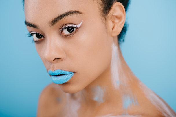 Detailní portrét ženy s kreativní make-up při pohledu na fotoaparát izolované na modré - Fotografie, Obrázek