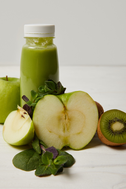 láhev zelené detoxikační koktejl s mátou a jablka, kiwi a na bílý dřevěný povrch    - Fotografie, Obrázek