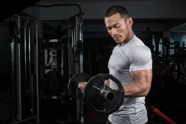 Muscular builder man training his body with barbell in Modern fitness center - Valokuva, kuva