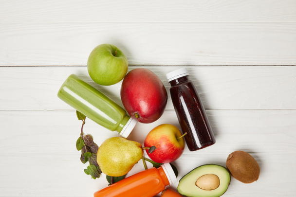 Draufsicht auf frisches Obst und Detox-Smoothies auf weißem Holzhintergrund   - Foto, Bild
