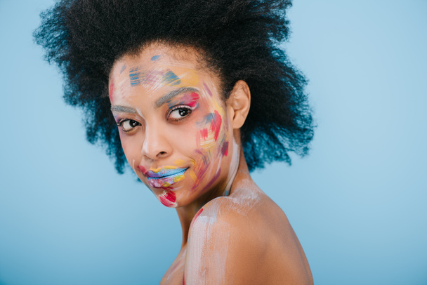 smiling young woman with paint strokes on face isolated on blue - Foto, immagini