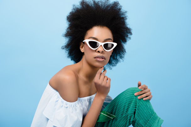 attractive young woman in stylish off-the-shoulder top and sunglasses isolated on blue - Zdjęcie, obraz
