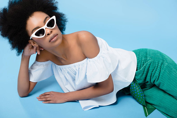 beautiful young woman in stylish clothes and sunglasses lying on floor on blue - Fotografie, Obrázek