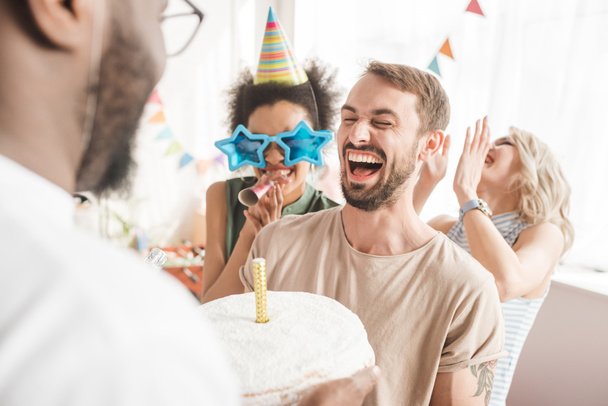 Amis multiraciaux saluant jeune homme avec gâteau d'anniversaire
 - Photo, image