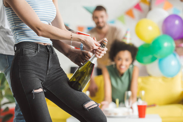 Vista de cerca del hombre ayudando a la mujer a abrir champán en la fiesta de cumpleaños
 - Foto, imagen