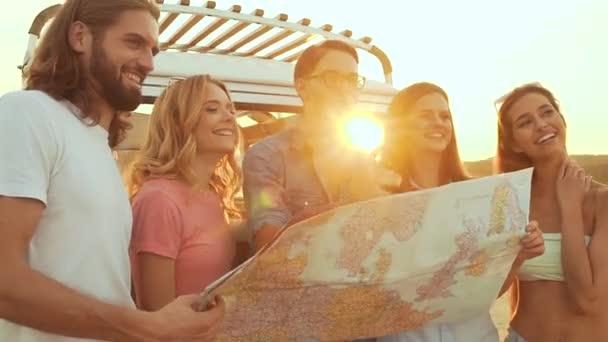 Summer Travel. Friends Using Map Near Car In Nature. Happy Smiling People Traveling In Bus On Weekend Vacation. Beautiful Young Men And Women Holding Map, Exploring Location On Trip. - Footage, Video