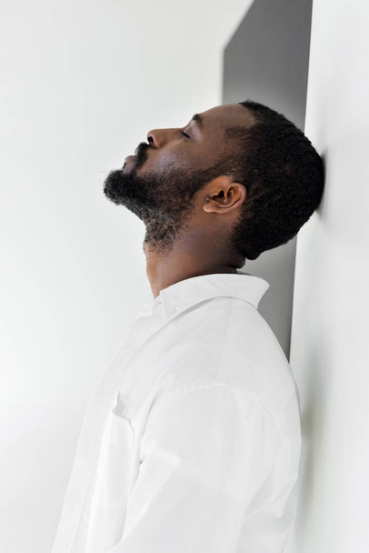 Widok z boku przystojny stylowy african american człowieka w białe szaty, opierając się na ścianie z zamkniętymi oczami - Zdjęcie, obraz
