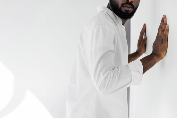 Oříznout obrázek stylových afroamerické muže v bílých šatech dotýká zdi - Fotografie, Obrázek