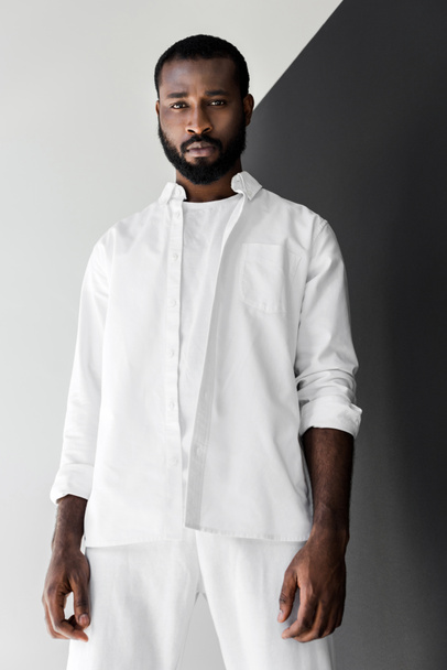 nízký úhel pohledu hezký stylový afroamerické muže při pohledu na fotoaparát v bílých šatech - Fotografie, Obrázek