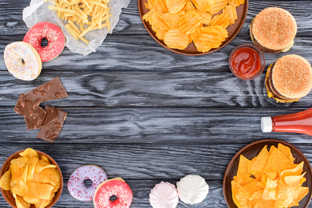 Draufsicht auf verschiedene Junk Food und Süßigkeiten auf Holztisch  - Foto, Bild
