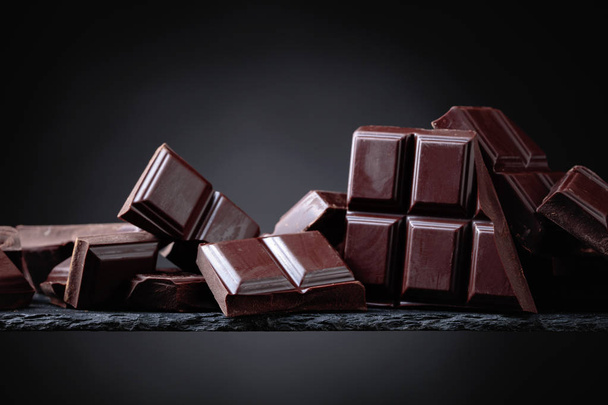 Potłuczone kawałki czekolady na czarnym tle. - Zdjęcie, obraz