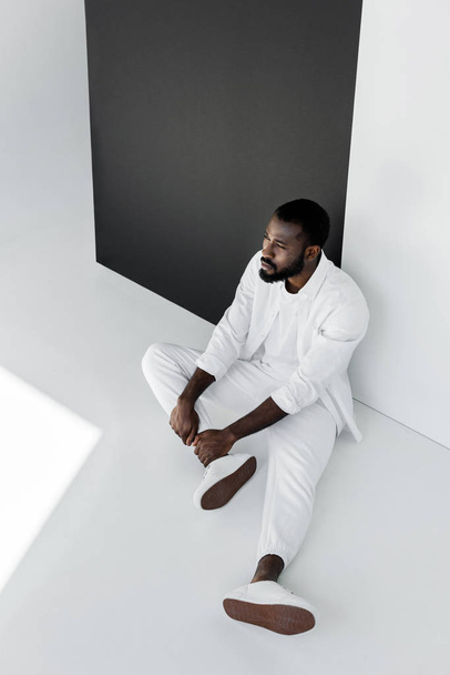 high angle view of handsome stylish african american man sitting on floor in white clothes - Photo, Image