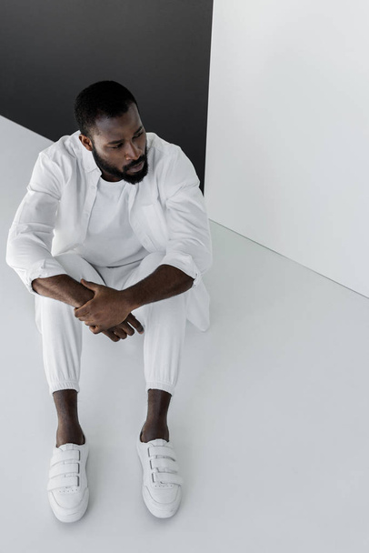 high angle view of handsome stylish african american man sitting in white clothes on floor - Photo, Image