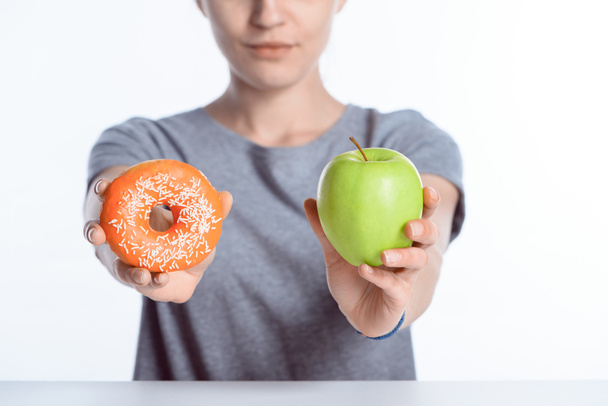Обрізаний знімок дівчини, що тримає свіже яблуко і пончик
 - Фото, зображення