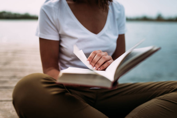 Close up van vrouw lezen van een boek buiten, naast het meer. - Foto, afbeelding