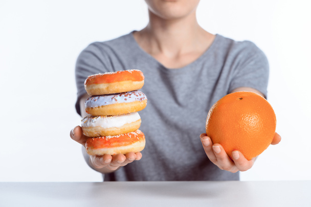 cropped shot of girl holding ripe orange and sweet donuts - Photo, Image