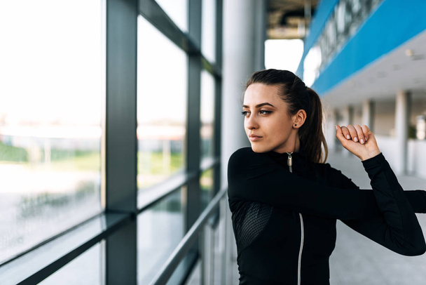 Concentrated slim woman in sports clothing stretching her arms standing near the window. - Fotoğraf, Görsel