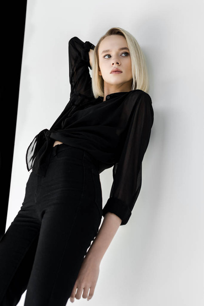 vonzó stílusos szőke nő pózol fekete ruhát fal mellett alacsony szög, kilátás - Fotó, kép
