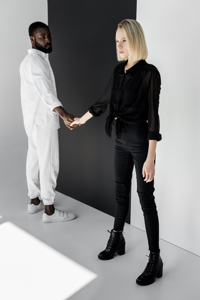 coppia multiculturale che si tiene per mano vicino alla parete in bianco e nero
 - Foto, immagini