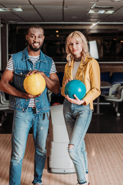felice giovane coppia con palle da bowling guardando la fotocamera al club
 - Foto, immagini