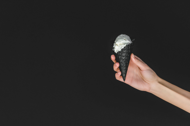 cropped image of woman holding ice cream in black cone isolated on black - Zdjęcie, obraz