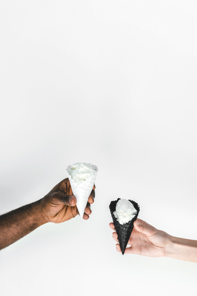 cropped image of multicultural couple holding ice cream cones isolated on white - Zdjęcie, obraz