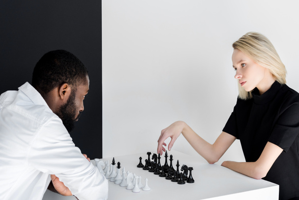 coppia multiculturale che gioca a scacchi vicino alla parete in bianco e nero
 - Foto, immagini