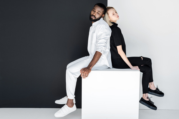 african american boyfriend and blonde girlfriend sitting back to back on white cube - Foto, Imagem