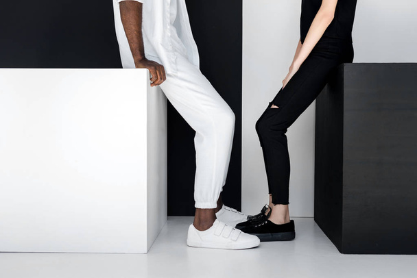 cropped image of african american boyfriend and girlfriend sitting on black and white cubes - Foto, Imagem