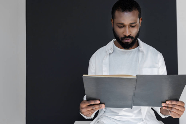 handsome stylish african american man in white clothes reading black book - Photo, image