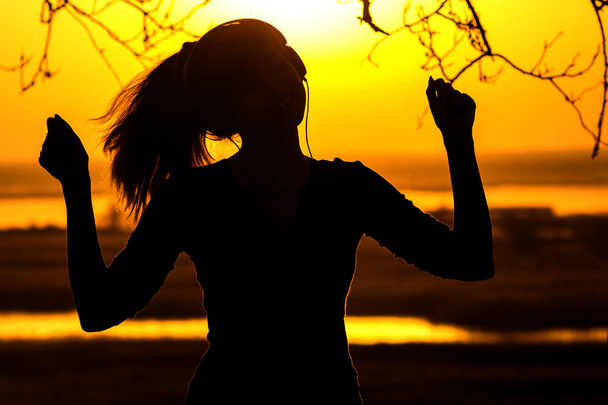 Silhouette einer Frau mit Kopfhörer, das Mädchen genießt Musik im Sonnenuntergang - Foto, Bild