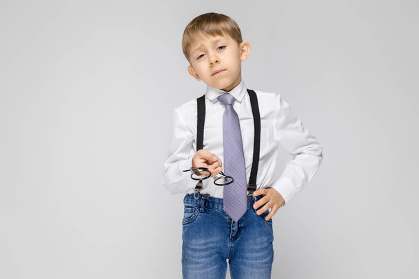 Portrait of adorable serious confident little boy wearing trousers with suspenders on grey background - Foto, Imagen