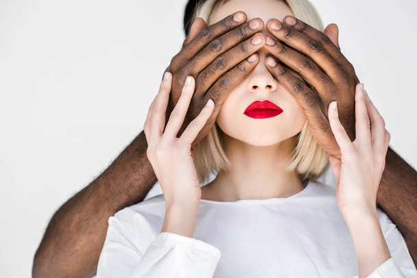 cropped image of african american boyfriend closing eyes of blonde girlfriend isolated on white - 写真・画像