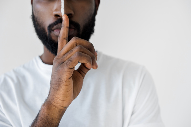 zugeschnittenes Bild eines afrikanisch-amerikanischen Mannes mit weißem Streifen im Gesicht, das Schweigezeichen isoliert auf weißem Grund zeigt - Foto, Bild