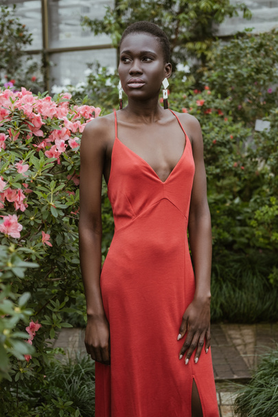 attractive african american girl with short hair in red dress posing in garden with flowers  - Fotoğraf, Görsel