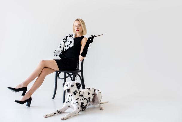 vonzó stílusos szőke nő ül a székre, a padlón fekvő dalmát kutya fekete ruha - Fotó, kép