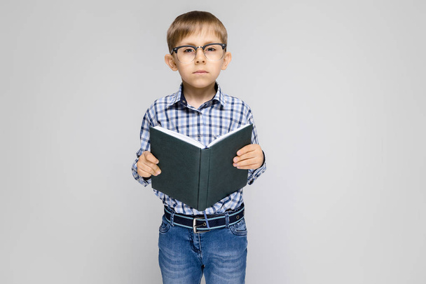 Portrait of adorable little boy in glasses holding book on grey background - Foto, afbeelding