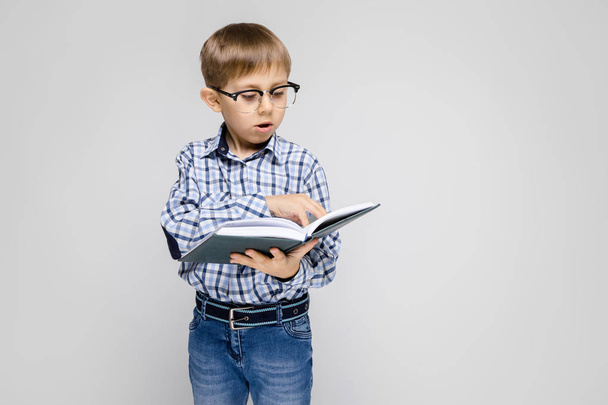 Portrait of adorable serious confident little boy in glasses reading book on grey background - Photo, Image