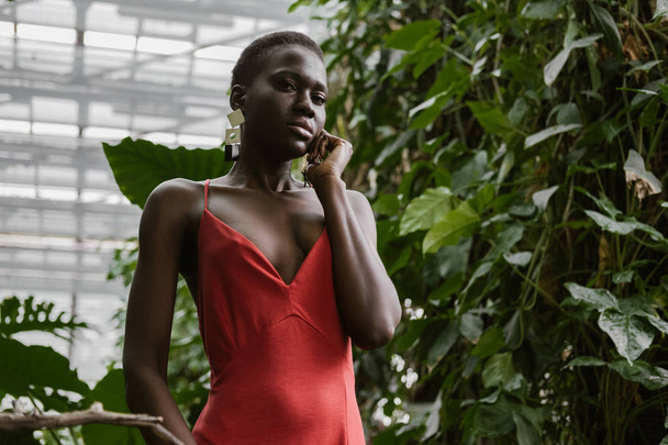 elegante afrikanisch-amerikanische Mädchen posiert in rotem Kleid im tropischen Garten - Foto, Bild