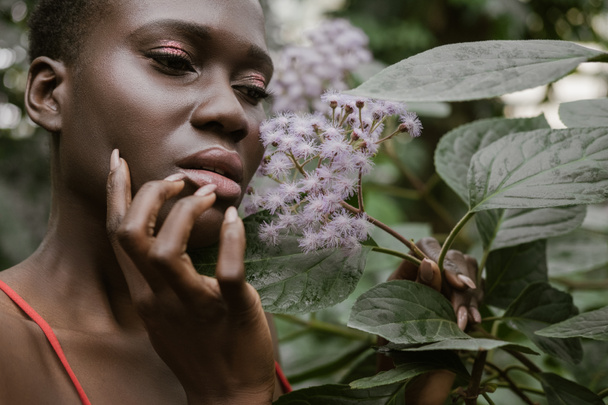 stylish african american woman with glitter eyeshadow posing with flowers - Photo, Image